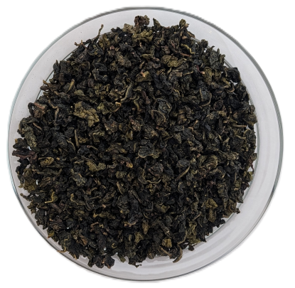 Dunkelgrüne, kugelig gerollte Oolong-Teeblätter, dicht gepackt in einer klaren Glasschale, aufgenommen aus der Vogelperspektive vor weißem Hintergrund.