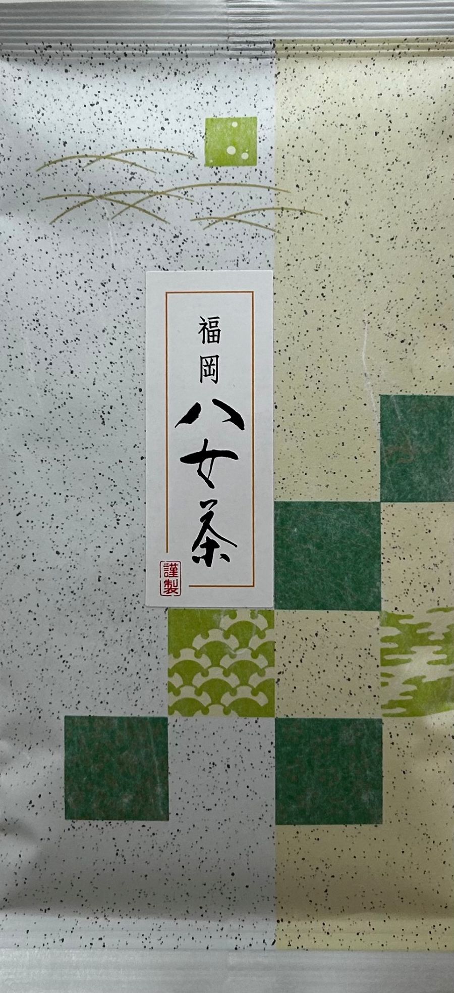 Vertikal zweigeteilte japanische Teeverpackung für den tiefgedämpften Grüntee Fukamushi-Cha aus Fukuoka Yame. Der Hintergrund ist weiß und beige mit einer feinen, dunklen Sprenkelung (Washi-Papier-Stil). Die rechte Seite ist im unteren Bereich mit einem g