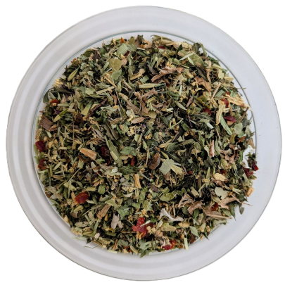 Draufsicht auf eine klare Glasschale mit losem Kräutertee. Die feine Kräutermischung enthält viele grün-graue, längliche Blatt- und Stängelstücke. Dazwischen blitzen kleine rote Hagebutten- oder Beerenstücke sowie zarte, gelbliche Blütenfäden hervor.