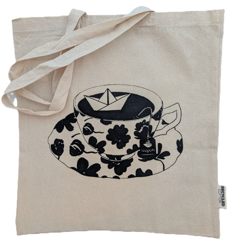 Naturweiße Tasche aus recycelter Baumwolle mit schwarzem Siebdruck-Design: Teetasse mit schwimmendem Papierboot und Teepott-Logo.