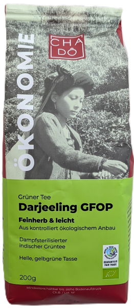 Cha Dô Ökonomie Bio Darjeeling GFOP Grüner Tee Verpackung in Frischem Grün mit Porträt einer indischen Teepflückerin. Bildbeschreibung: Standbeutel mit leuchtend grünem Etikett, Schwarz-Weiß-Fotografie einer jungen indischen Frau im Teefeld und Fairtrade-