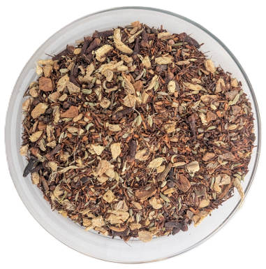 Eine Schale mit loser Rooibos-Gewürztee-Mischung, enthaltend grobe Ingwerstücke, ganze Nelken, Fenchelsamen und Anis, fotografiert von oben auf weißem Grund.